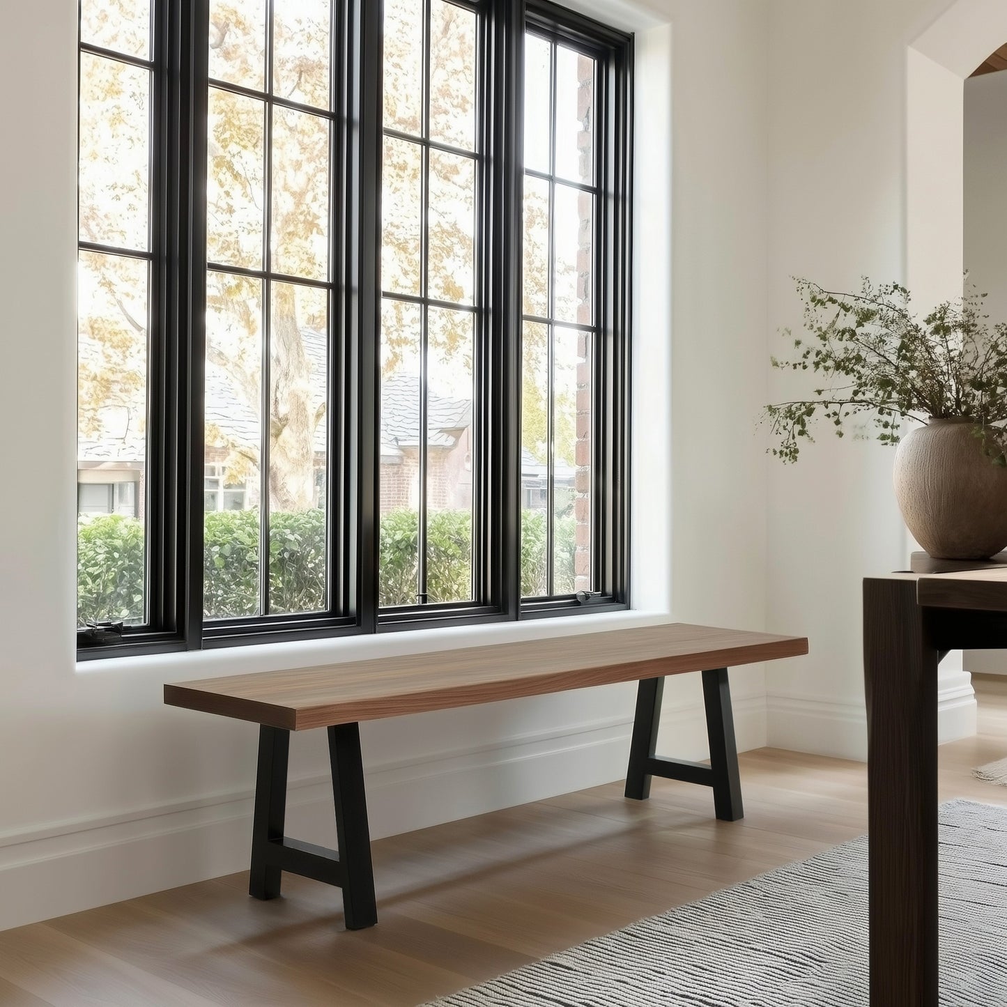 Wooden bench in a room with large windows and a vase of flowers on a table.