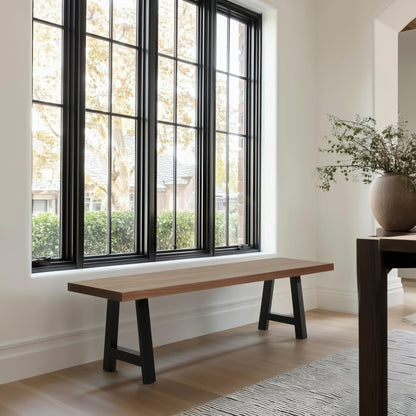 Wooden bench in a room with large windows and a vase of flowers on a table.