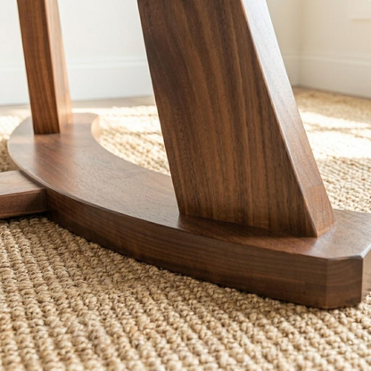 Close-up of a dark brown wooden table base or chair leg resting on a woven beige rug in a bright indoor setting.