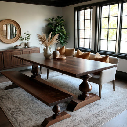 Wooden dining table with benches in a room with large windows and decorative elements.