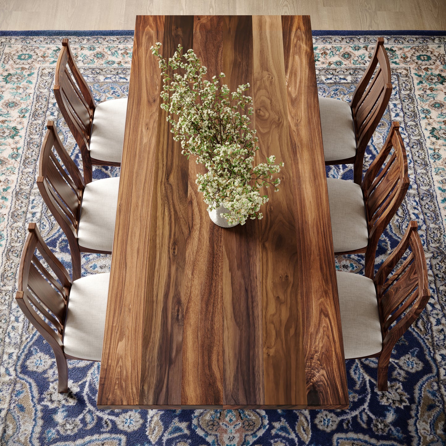 Top down view of a walnut dining table with turned wooden base featuring matching chairs in well lit dining room surrounded by large windows and a fireplace