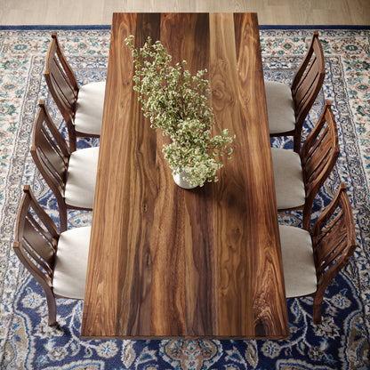 Top down view of a walnut dining table with turned wooden base featuring matching chairs in well lit dining room surrounded by large windows and a fireplace