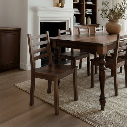Wooden dining table with chairs in a room with a fireplace and bookshelf.