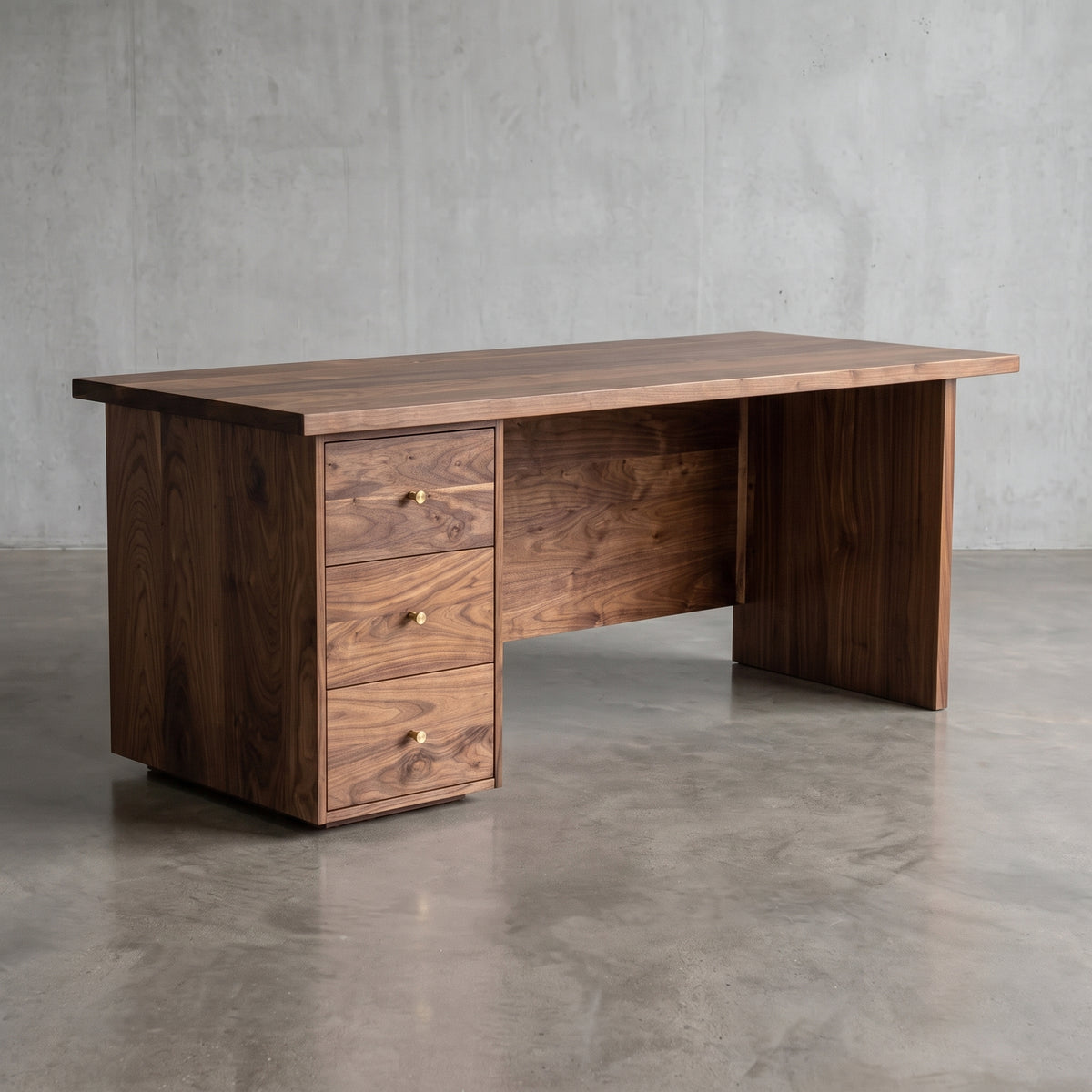 A dark brown wooden writing desk with three drawers on the left and a slatted back panel, set against a concrete wall and floor.