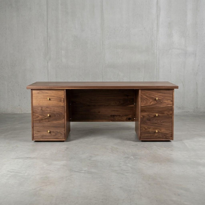 A dark brown wooden writing desk with three drawers on the left, three drawers on the right, and an open center space, set against a gray concrete wall and floor.