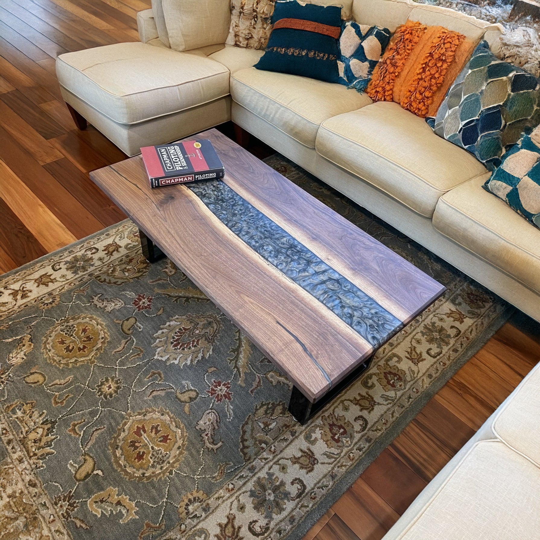 An epoxy coffee table with U-shape legs made of solid hardwood, placed on a patterned rug in a living room setting.