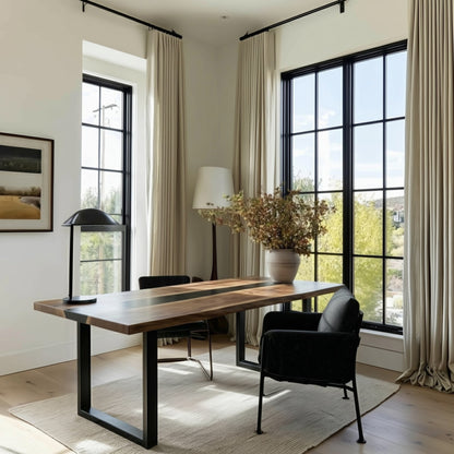 Modern interior with a wooden dining table and black chairs near large windows.