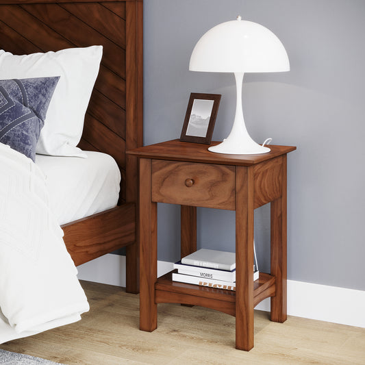 A shaker nightstand made of walnut featuring one drawer and one lower shelf in a well lit bedroom against a blue wall