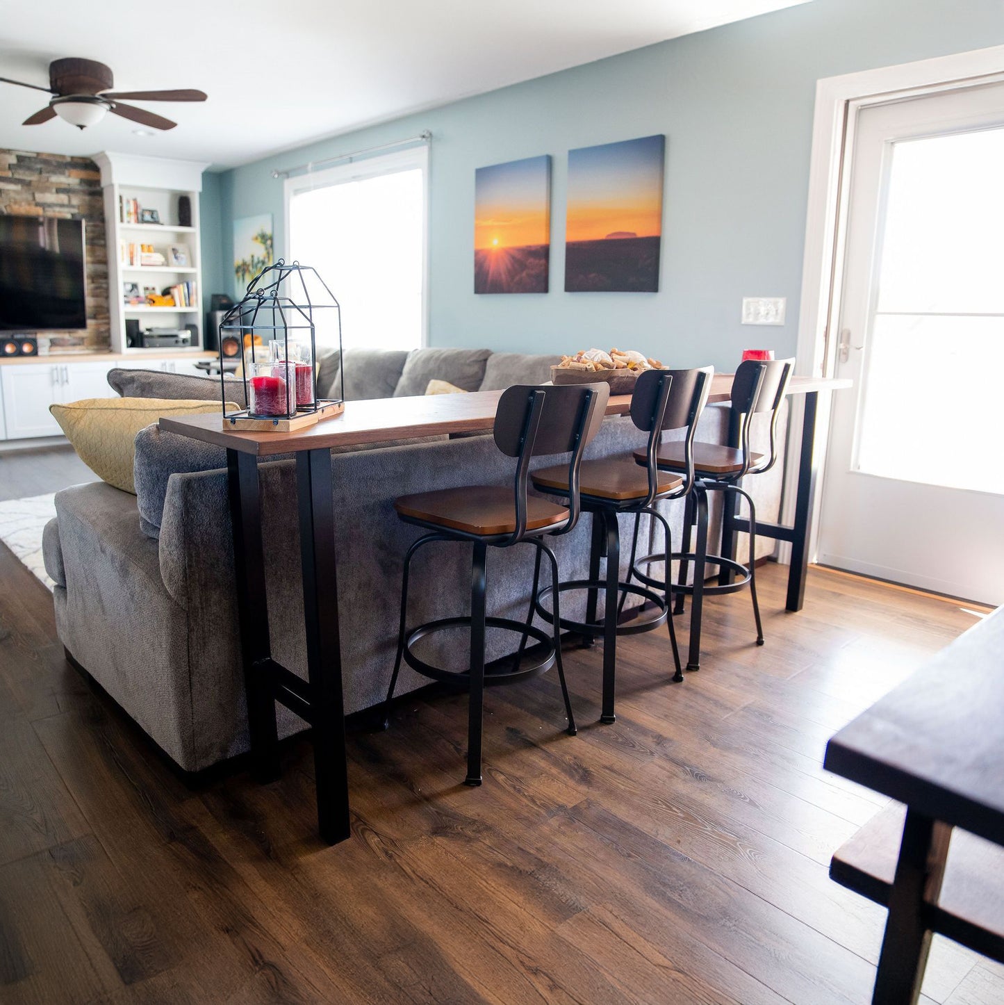 A walnut sofa table with a live edge design, featuring metal hairpin legs, placed in a living room setting with high-backed grey sofa and decorative cushions.