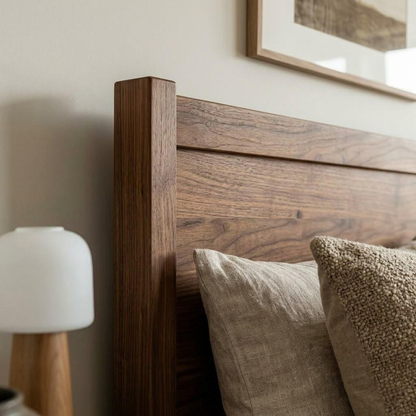 Close-up of a dark brown wooden bed headboard with textured beige and brown pillows in a softly lit bedroom setting.