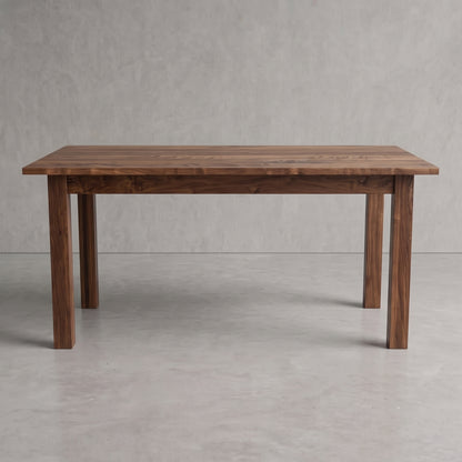 A rectangular wooden dining table with a dark brown walnut finish, featuring four sturdy legs and a thick tabletop, set against a neutral gray concrete floor and textured gray wall.