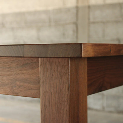A rectangular dining table with a dark wood finish and metal legs, placed on a concrete floor against a brick wall.