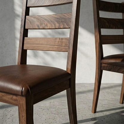 A close-up of a wooden dining chair with a brown leather seat cushion, shown in a modern interior setting with soft shadows on a light gray wall and concrete floor. Part of a second matching chair is visible on the right.