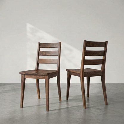 Two dark brown wooden dining chairs with ladder backs, shown from the rear in a minimalist studio setting with a gray concrete floor and a light gray wall.