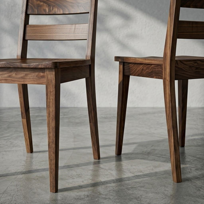 Two dark brown wooden dining chairs with a slatted backrest, shown in a minimalist studio setting with a textured gray concrete floor and wall.