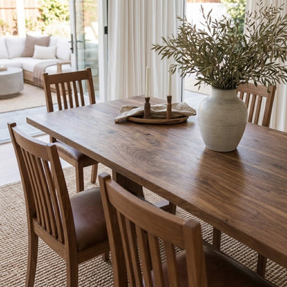 Walnut Rowland Dining Table with Ensworth Chairs, featuring rich natural wood grain, brown upholstered seats, and decorative greenery in a bright dining room.