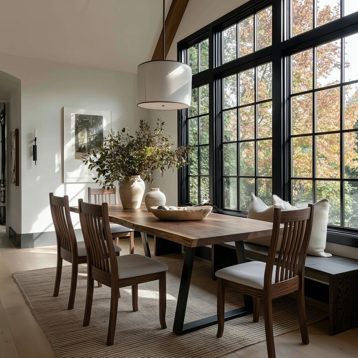 Dining room with wooden table and chairs near large windows with a view of trees.