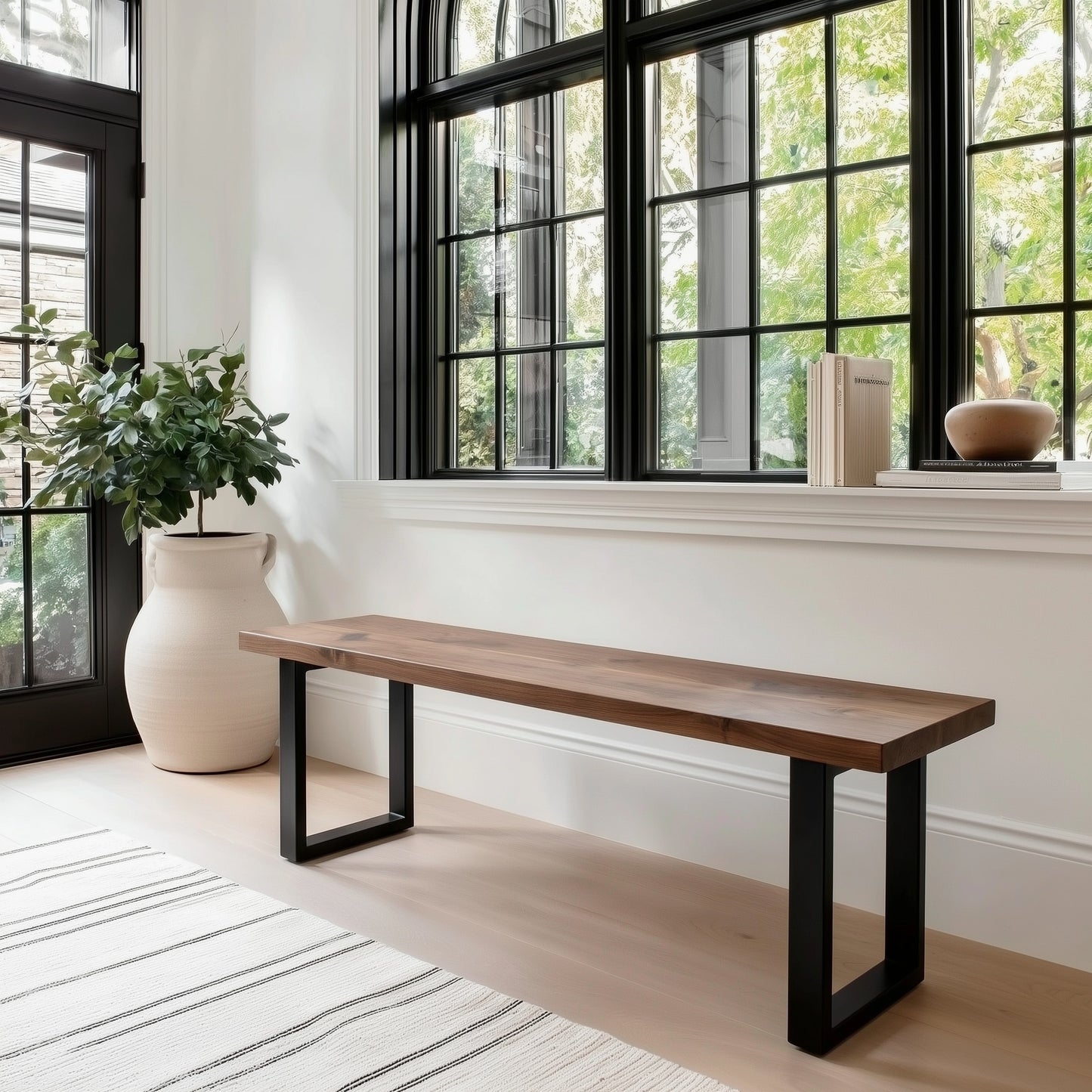 Wooden bench with black metal legs in a room with large windows and a plant.