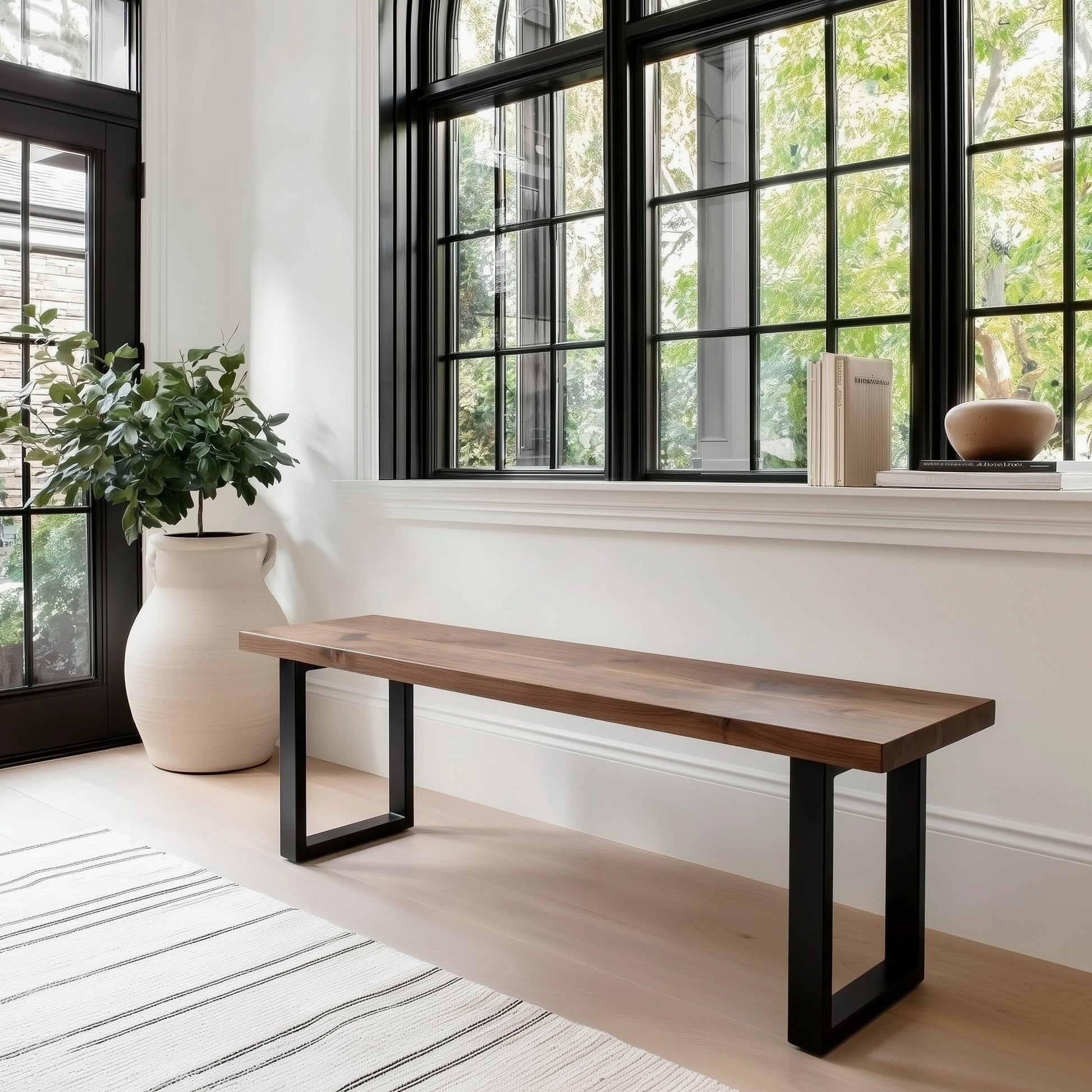 Wooden bench with black metal legs in a room with large windows and a plant.