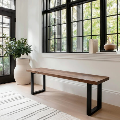 Wooden bench with black metal legs in a room with large windows and a plant.