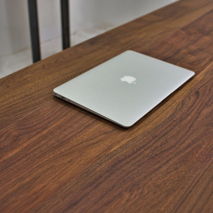 Close up of a walnut desk top with a laptop placed on it.