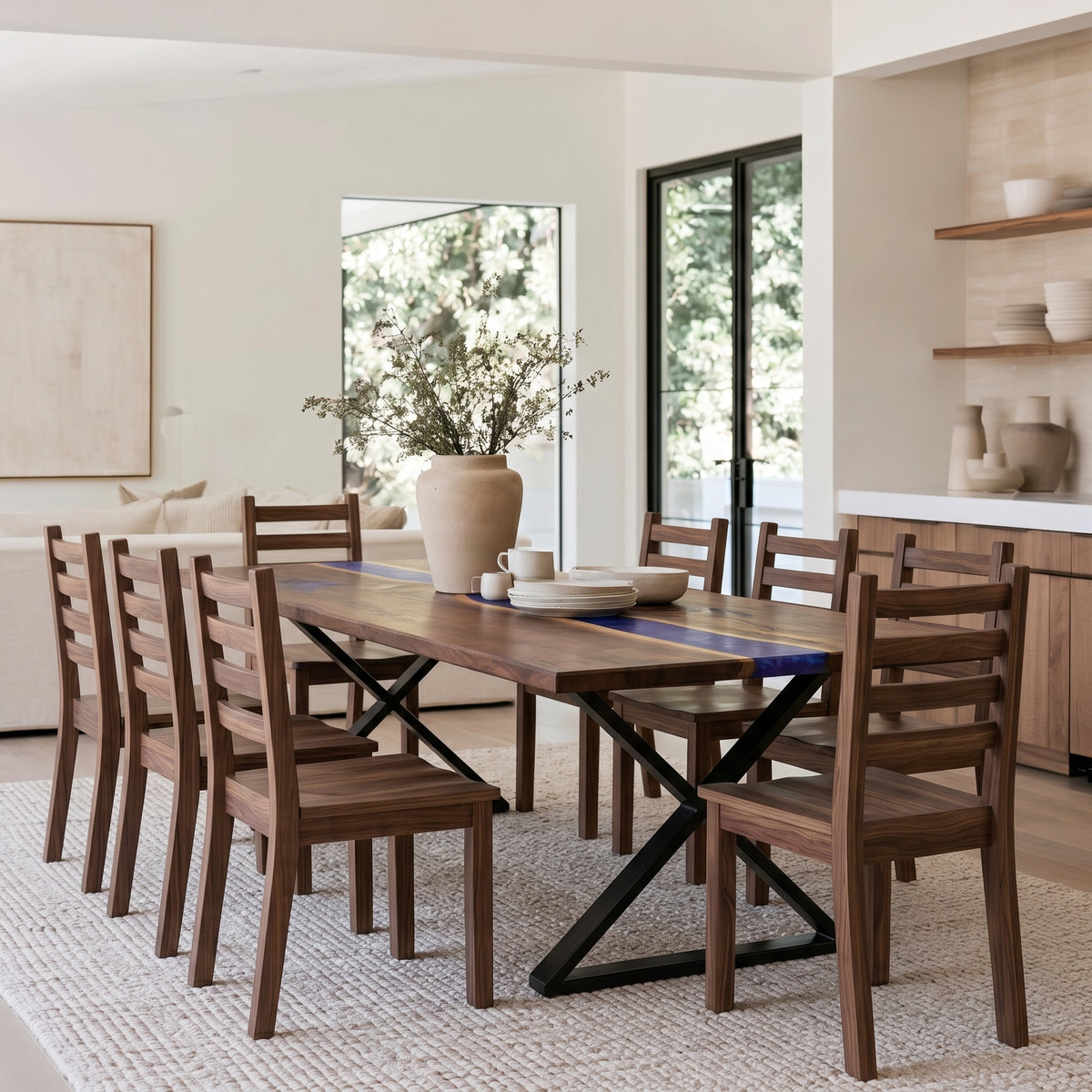 A modern dining room set featuring a rectangular wooden table with a blue inlay and black X-frame base, surrounded by matching wooden ladder-back chairs, set on a textured light rug in a bright, contemporary dining room.